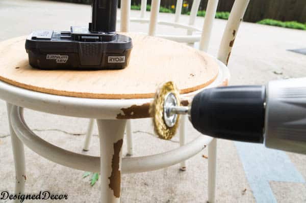 using an electric drill with round metal brush attachment to remove rust from metal chair