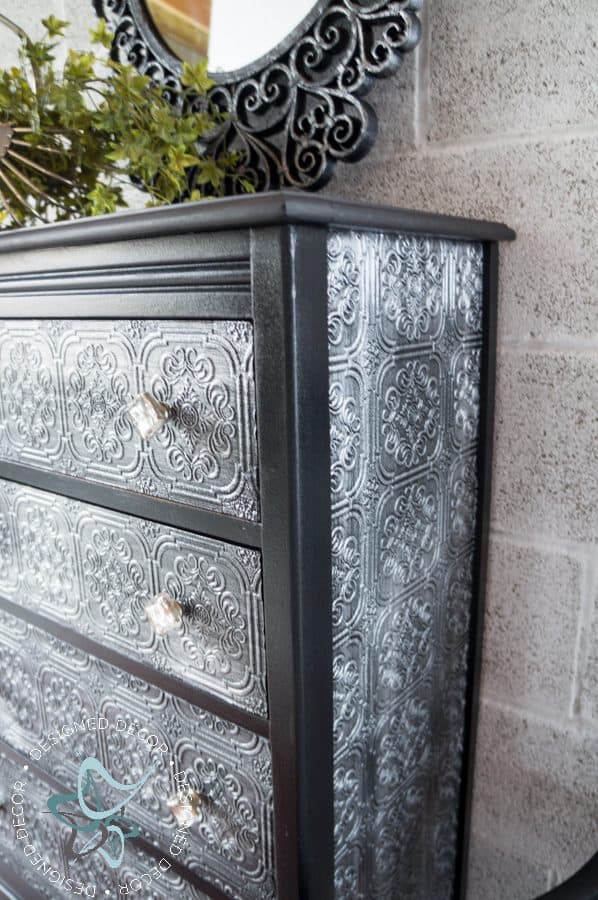 black painted dresser with metallic painted wallpaper on the sides and dresser drawer fronts