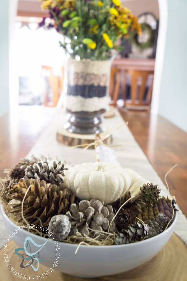 white bowl filled with pine cones and mini white pumpkins with fall floral centerpiece in the background