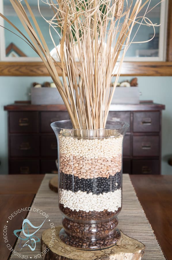 glass vase filled with layers of dried beans and dried fall floral