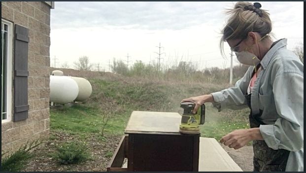 lady using a hand sander to strip furniture