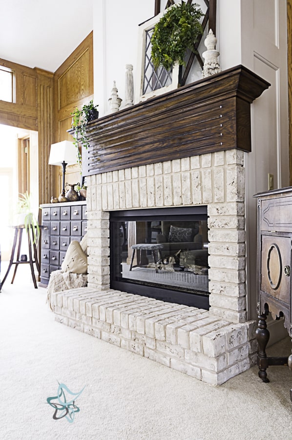 image of a decorated brick fireplace with a dark stained mantel and a white properly paint oak wall above the mantel