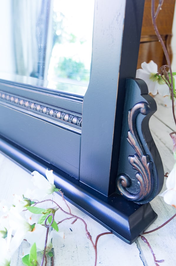 Close up image of a black painted mirror with light distressing on the carved details