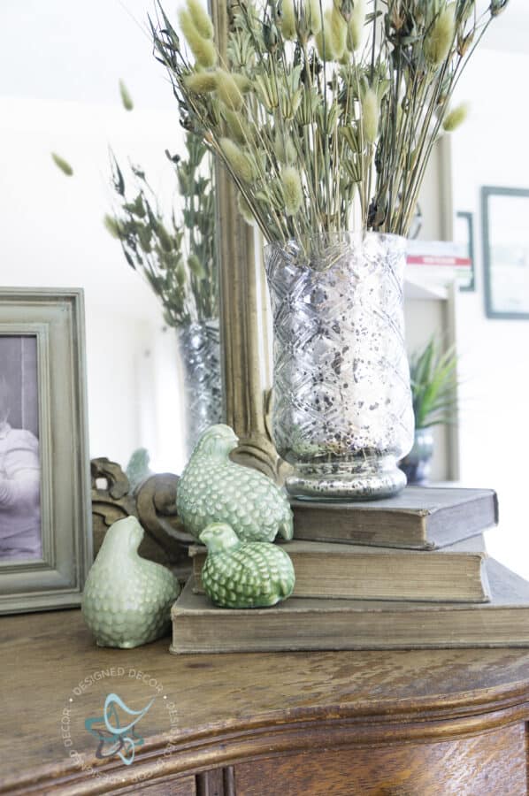 entryway table with ceramic birds on books and a vase of dried flowers