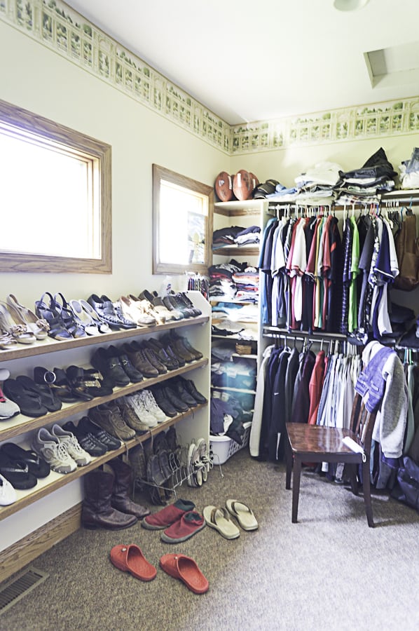 a cluttered walk-in closet with hanging and shoe shelves