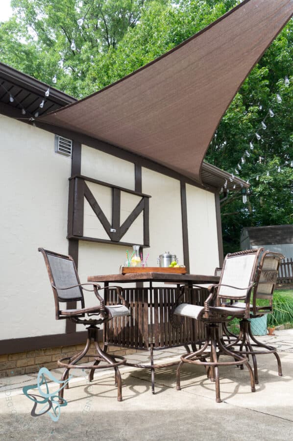 patio with a metal bar table and chairs with outdoor TV cabinet closed in the background